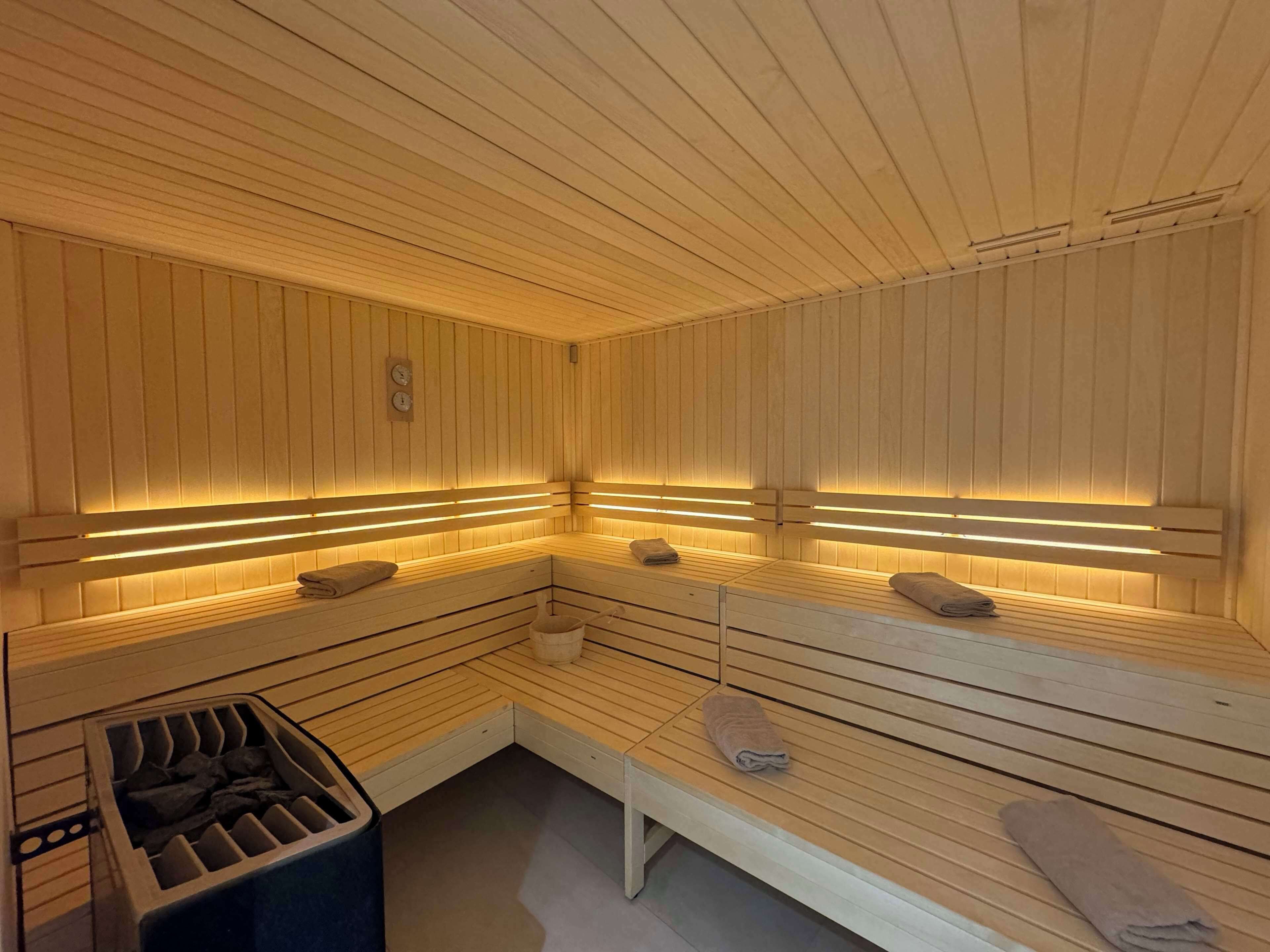 A sauna with wooden benches and benches, a bench with a towel, and a trash bin.