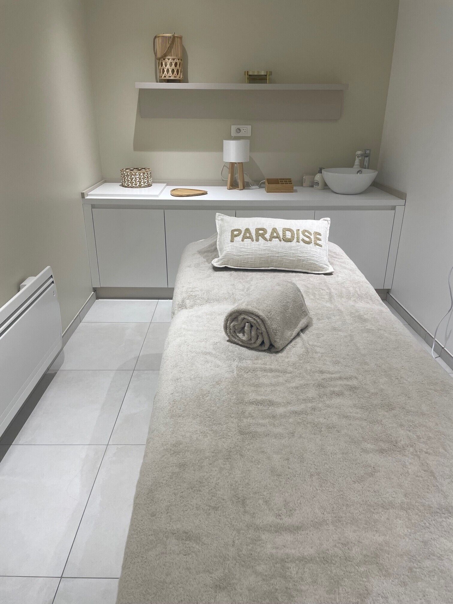 A bathroom with a white sink, a towel with 'PARADISE' on it, and a shelf with a lamp and decorative items.