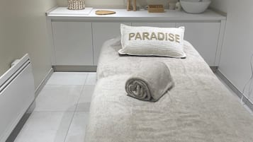 A bathroom with a white sink, a towel with 'PARADISE' on it, and a shelf with a lamp and decorative items.