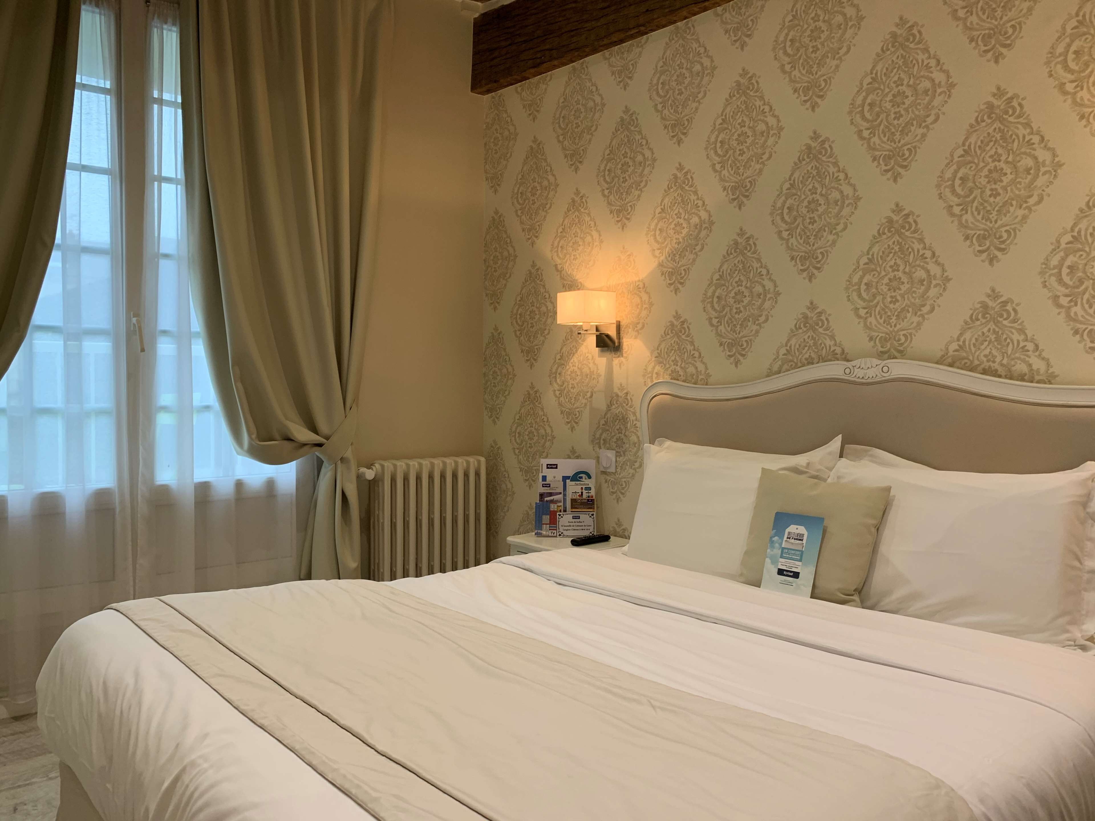 Una cama bien hecha con sábanas blancas, una mesita de noche con una lámpara y un papel tapiz estampado.