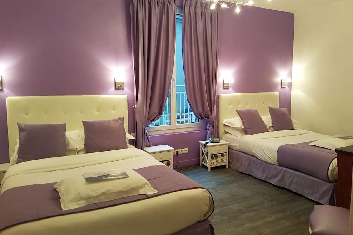 A hotel room with two beds, purple bedding, a window with curtains, bedside lamps, and a small table with a phone.