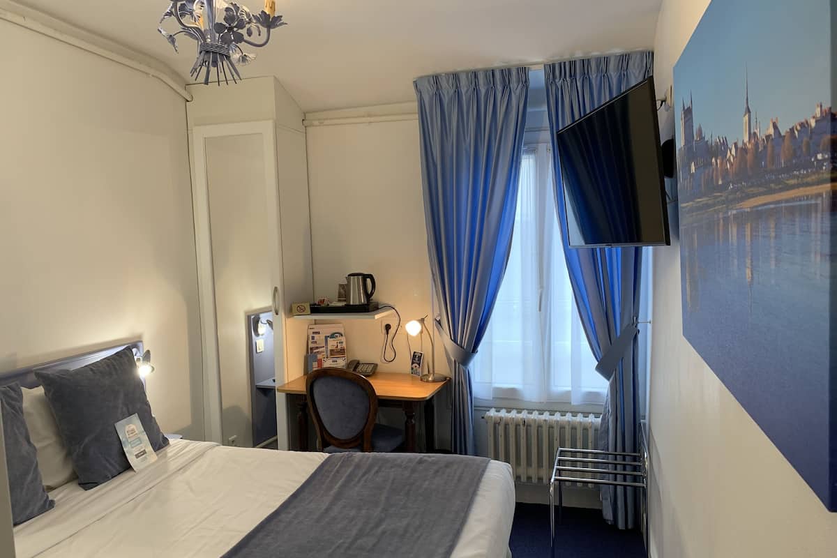 A hotel room with a bed, desk, chair, and a television mounted on the wall.