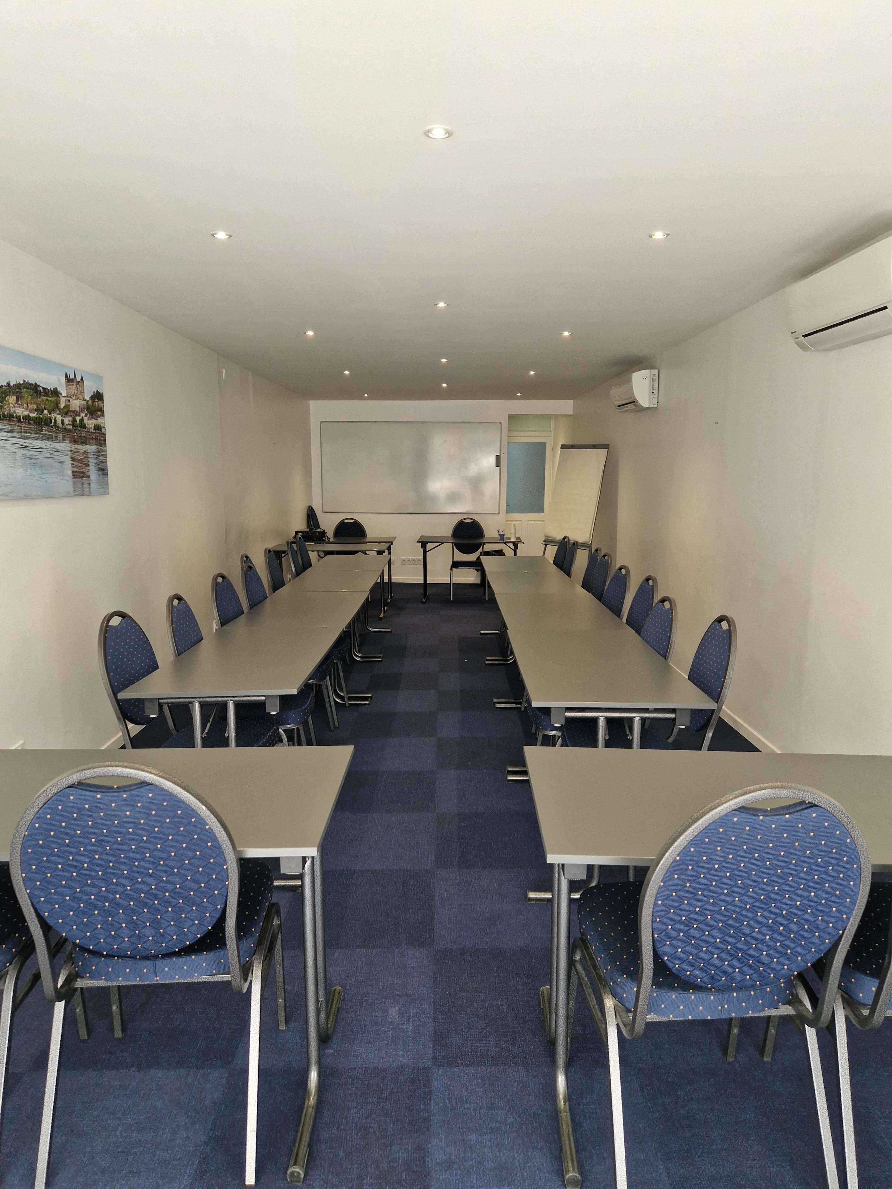 Une salle de conférence équipée d’une longue table, de chaises, d’un tableau blanc et d’un appareil de climatisation.