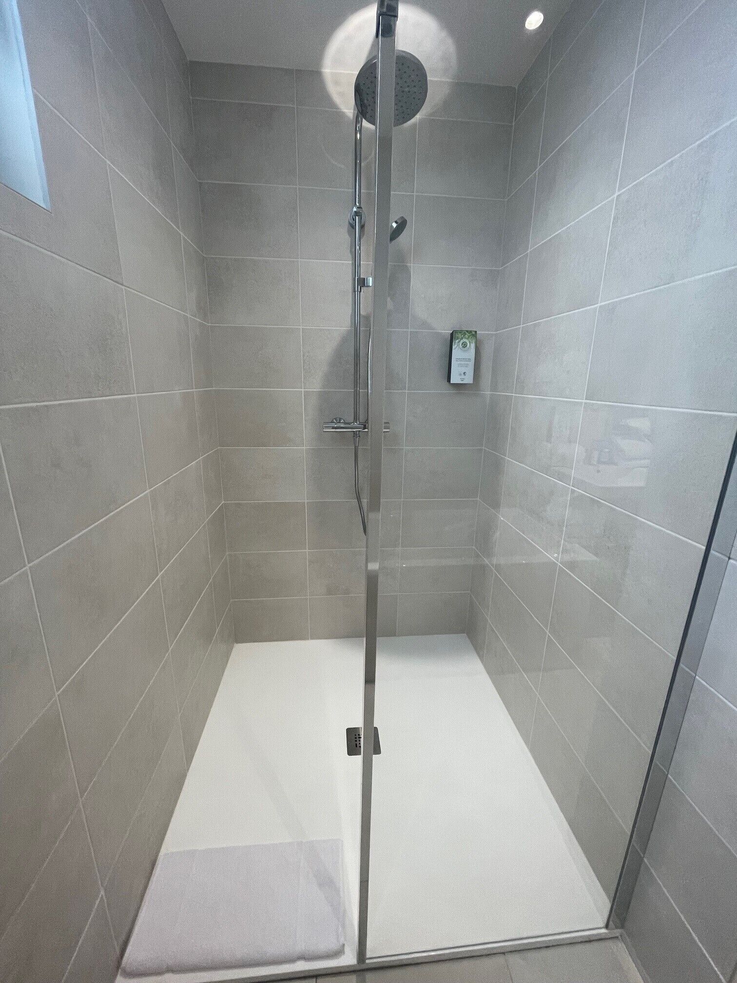 A modern shower stall with a glass door, grey tiles, and a control panel on the wall.