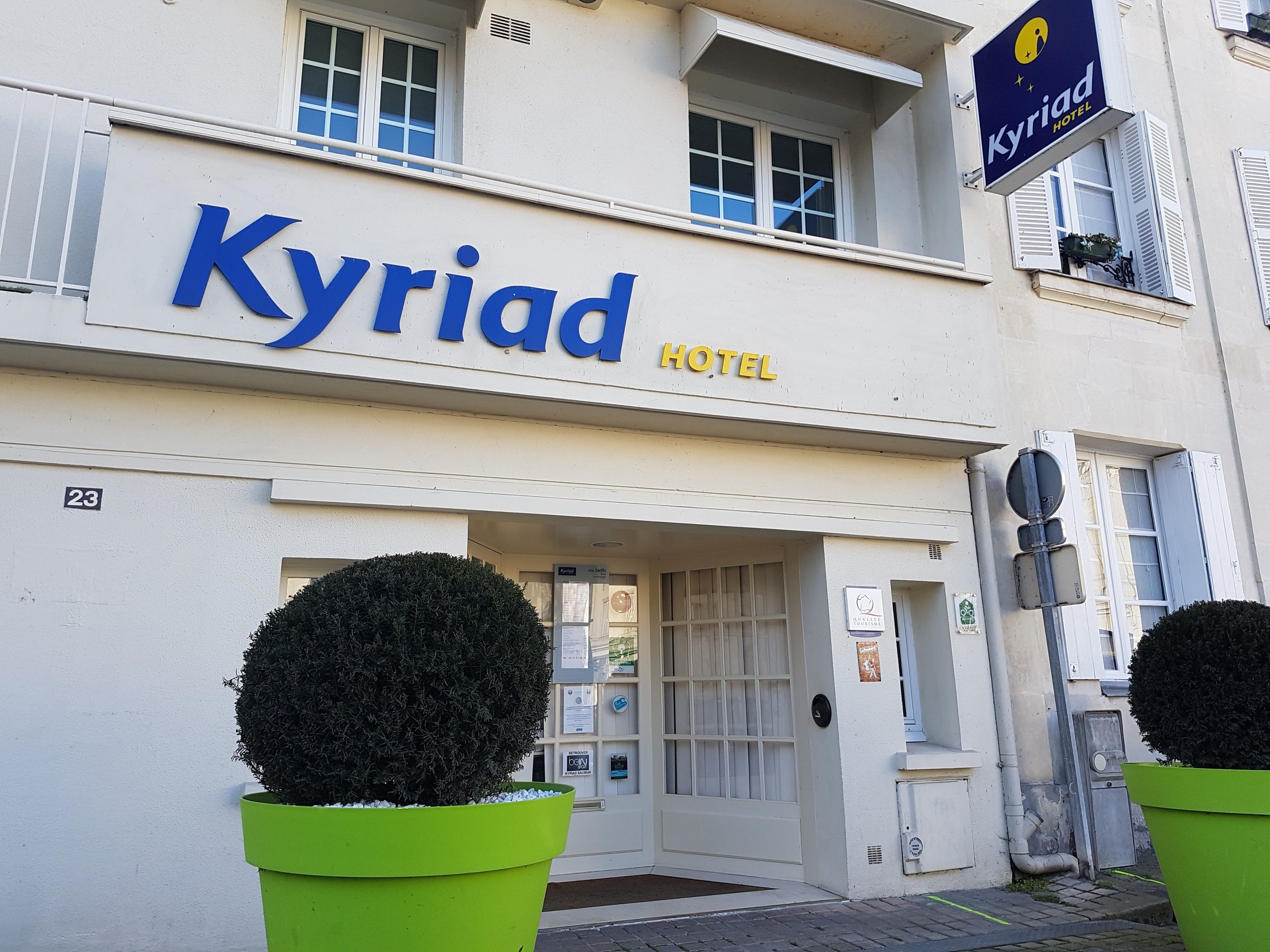 L’extérieur de l’hôtel Kyriad se distingue par une enseigne bien visible, le chiffre « 23 » apposé sur le bâtiment et deux arbustes taillés en forme de cône placés de part et d’autre de l’entrée.