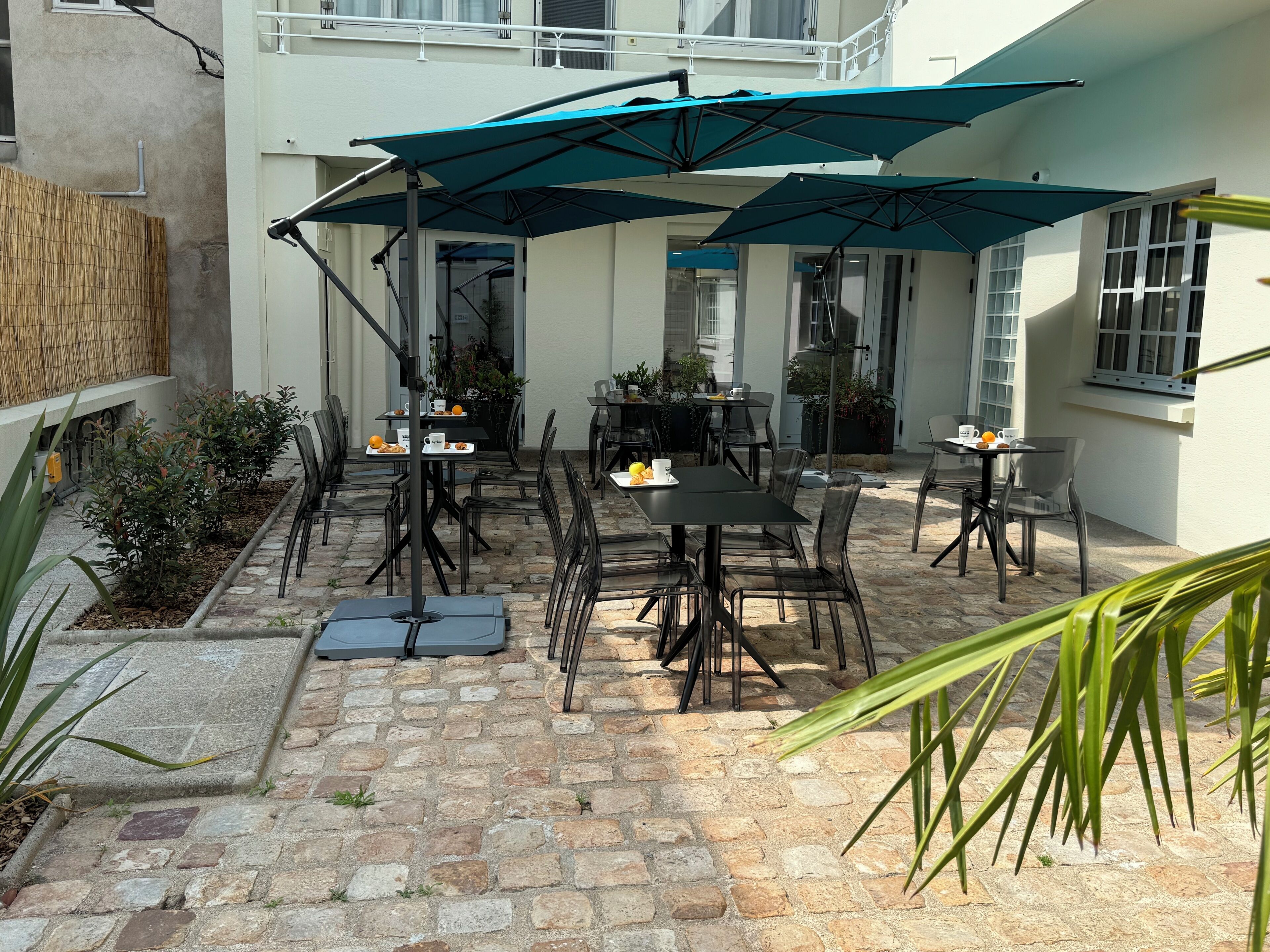 A patio area with stone flooring, outdoor tables and chairs, and umbrellas providing shade.
