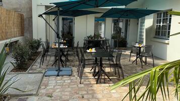 A patio area with stone flooring, outdoor tables and chairs, and umbrellas providing shade.