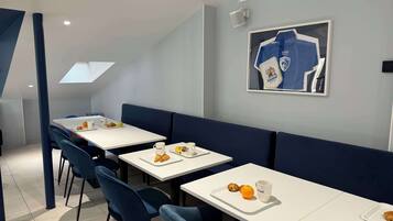 A modern dining area with white tables and blue chairs, featuring breakfast items like croissants and oranges.
