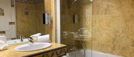 Un baño con tocador de mármol, un espejo grande, una bañera y una ducha con cerramiento de vidrio.