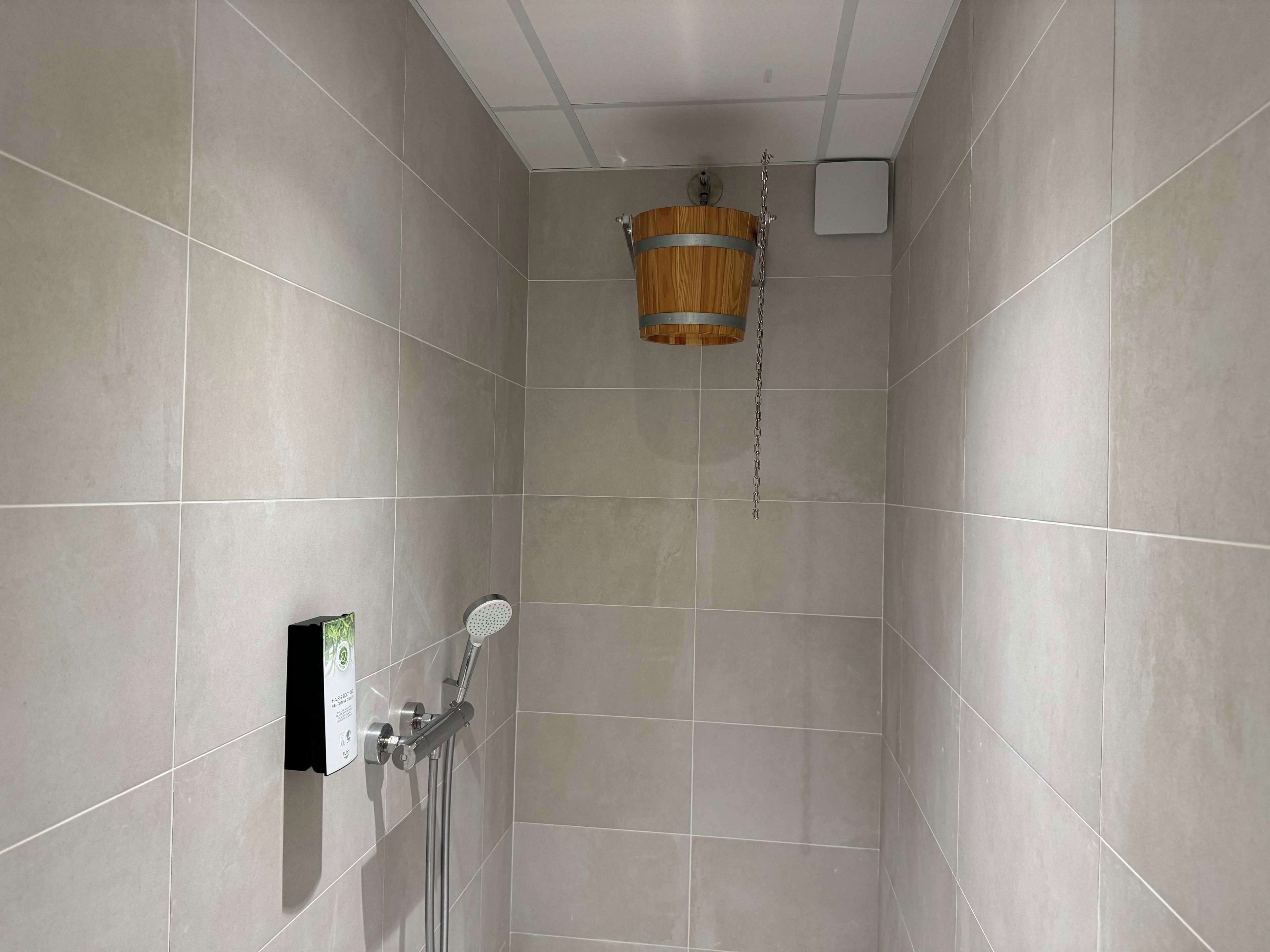 A shower with a wooden bucket, a handheld showerhead, and a wall-mounted control panel.