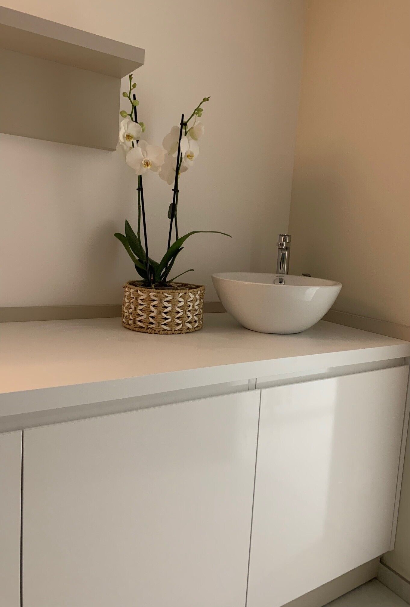 A bathroom with a white sink, a woven plant holder, and a white cabinet.
