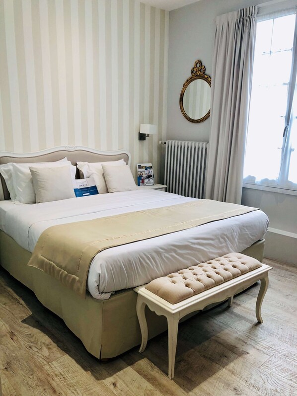 A neatly arranged bedroom with a large bed, a bedside table, a mirror, and a radiator. - Hotel Kyriad Saumur (Saumur)