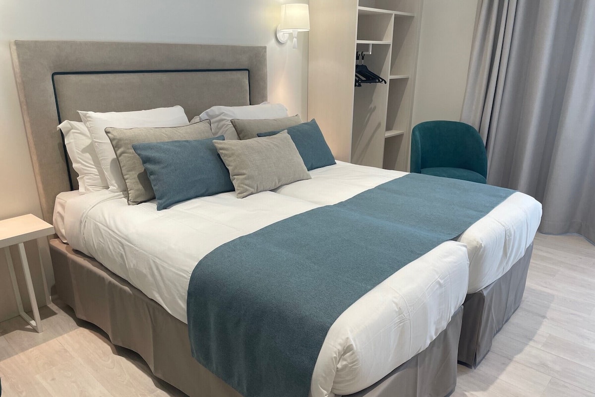 A neatly made bed with a grey headboard, white bedding, and blue accents.
