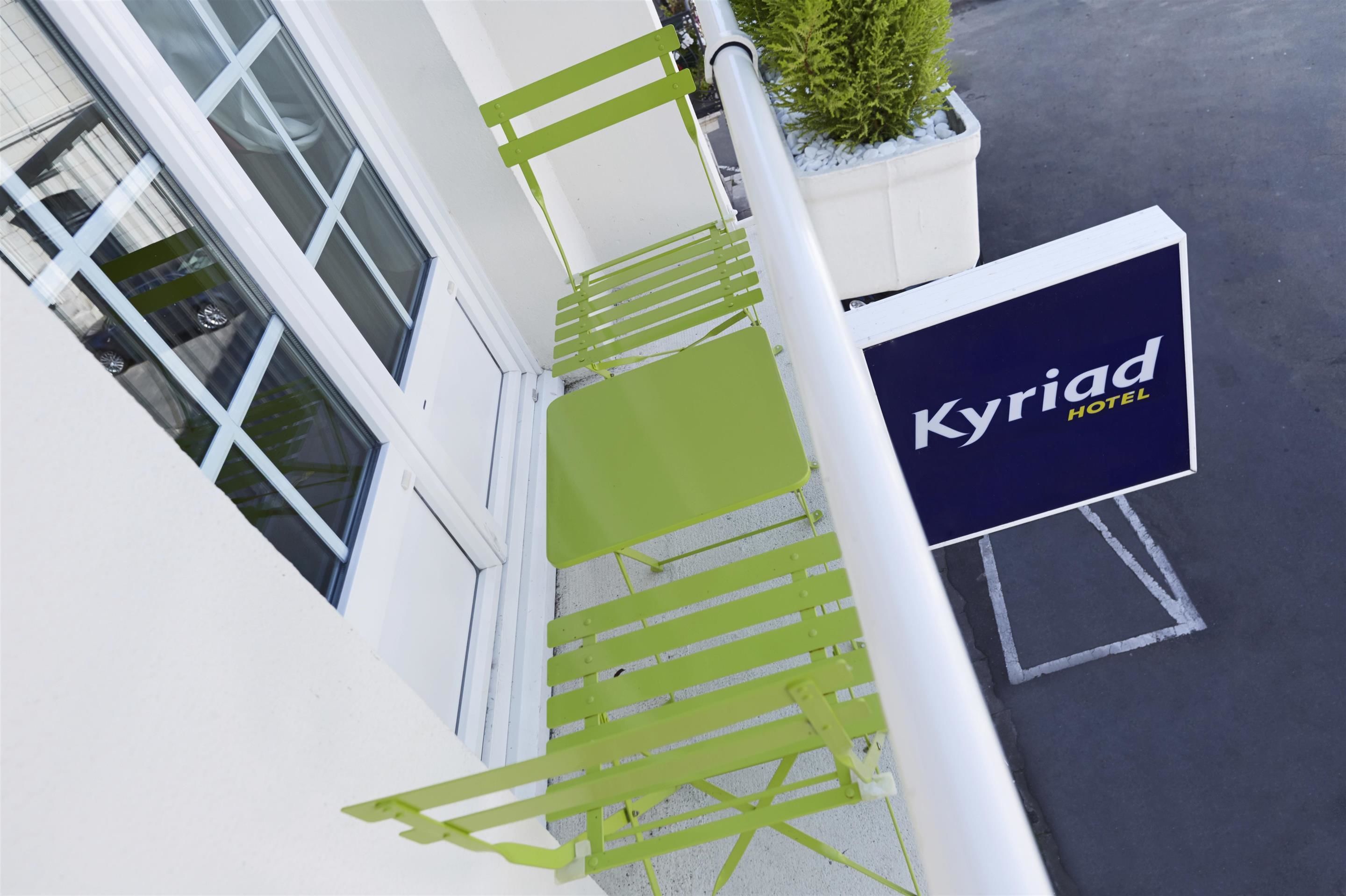 A hotel entrance with a green chair and a sign for 'Kyriad Hotel'.