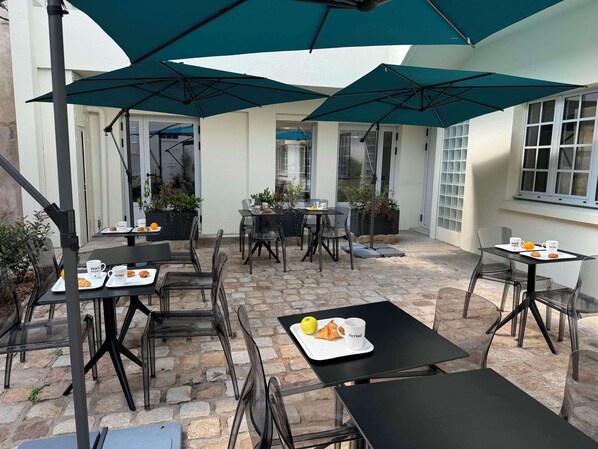 An outdoor patio area with tables and chairs, covered by large umbrellas, and surrounded by potted plants. - Hotel Kyriad Saumur (Saumur)