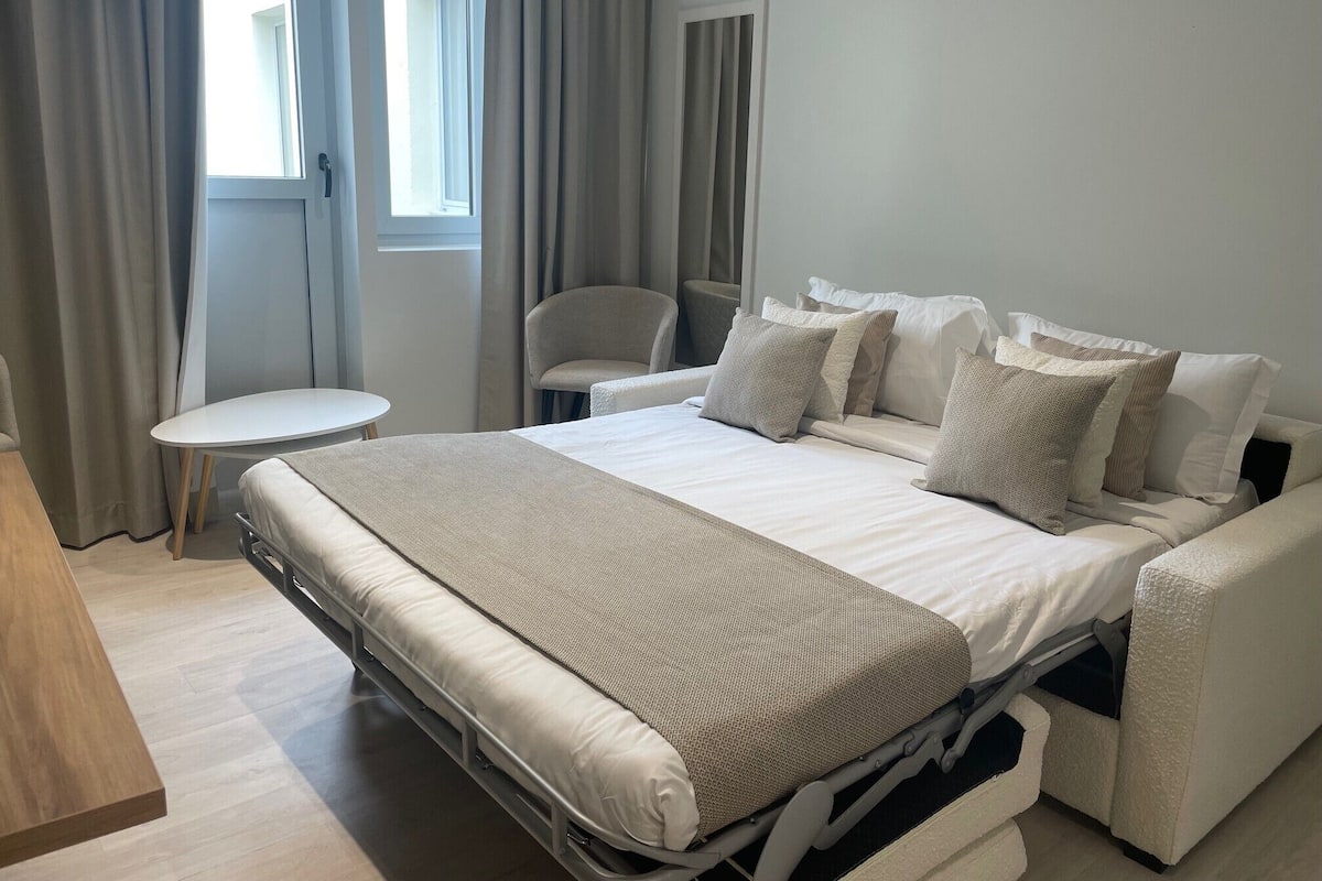 A modern hotel room with a bed, a small round table, and a chair.