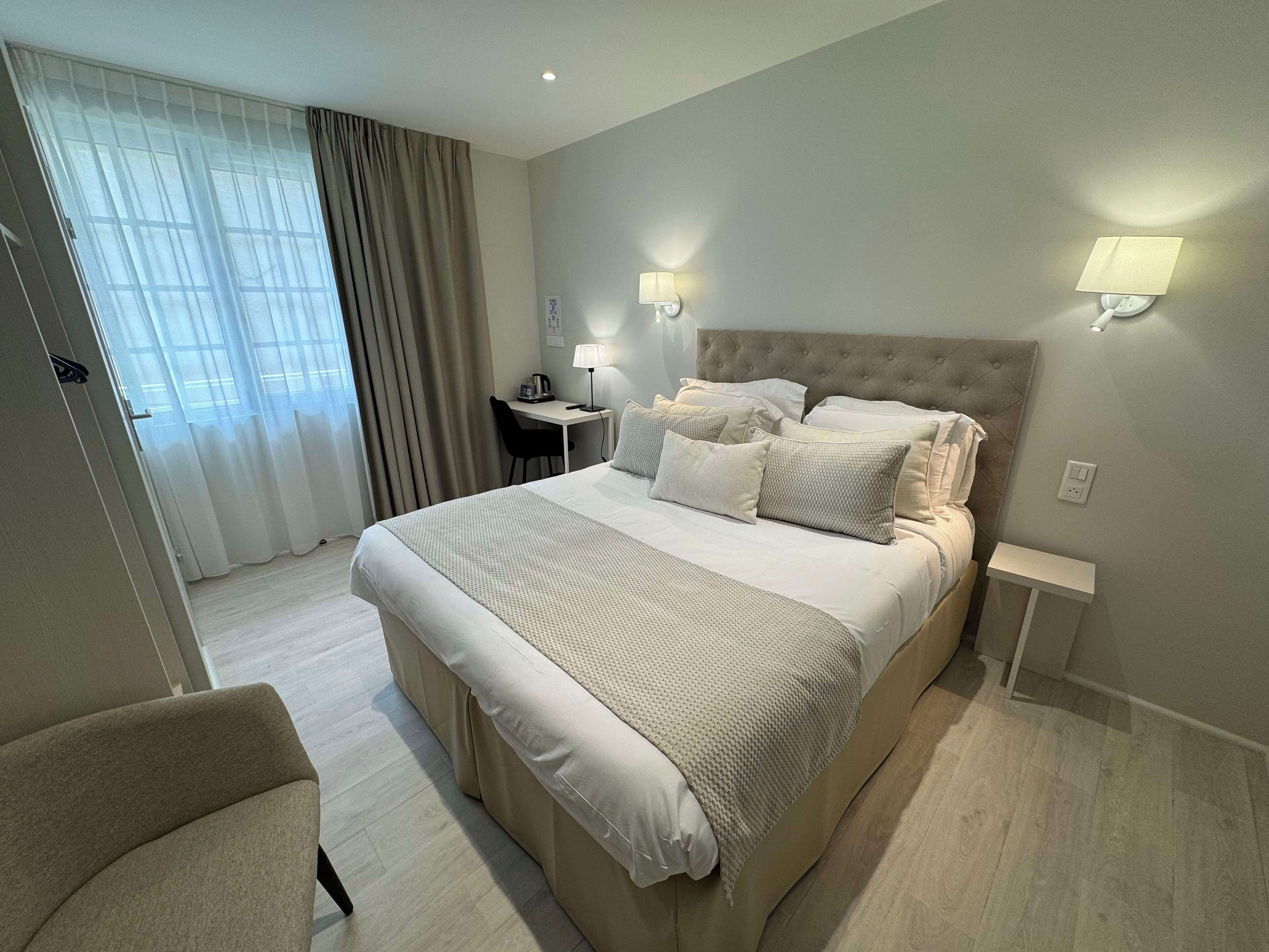 A hotel room with a large bed, a desk, a chair, and a window with curtains.