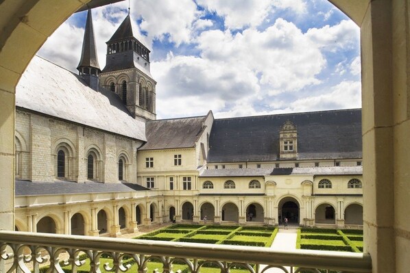Ein Innenhof mit symmetrischem Garten, ein großes Gebäude mit einem zentralen Turm und ein kleineres Gebäude mit einem geneigten Dach.