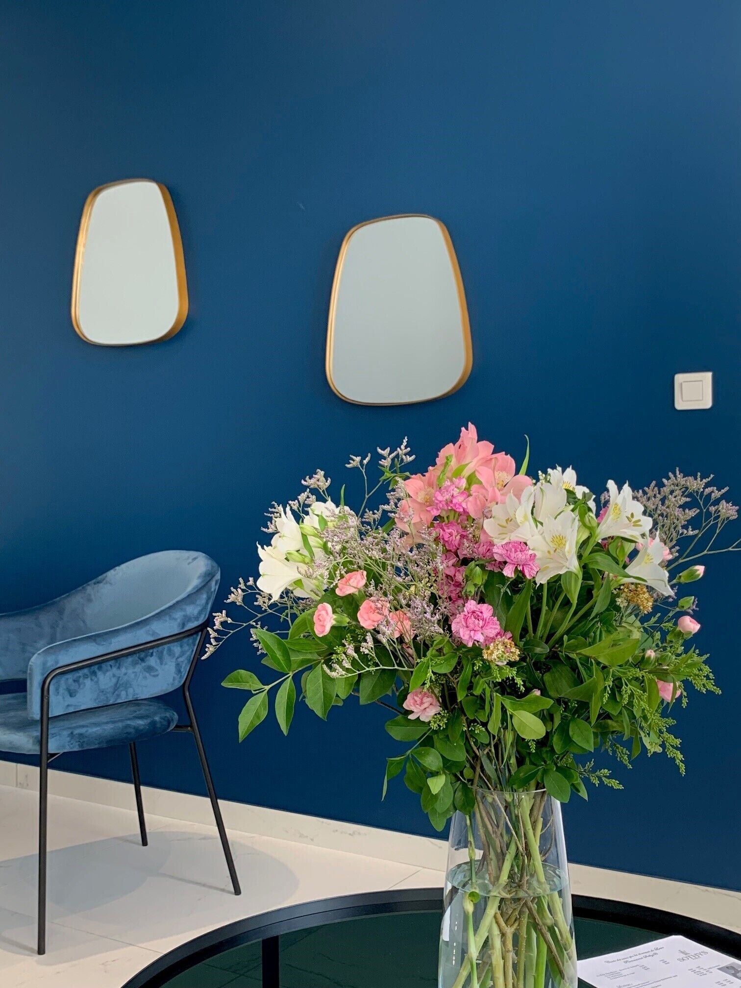 A room with a blue wall, a round table with a vase of flowers, and a blue chair.
