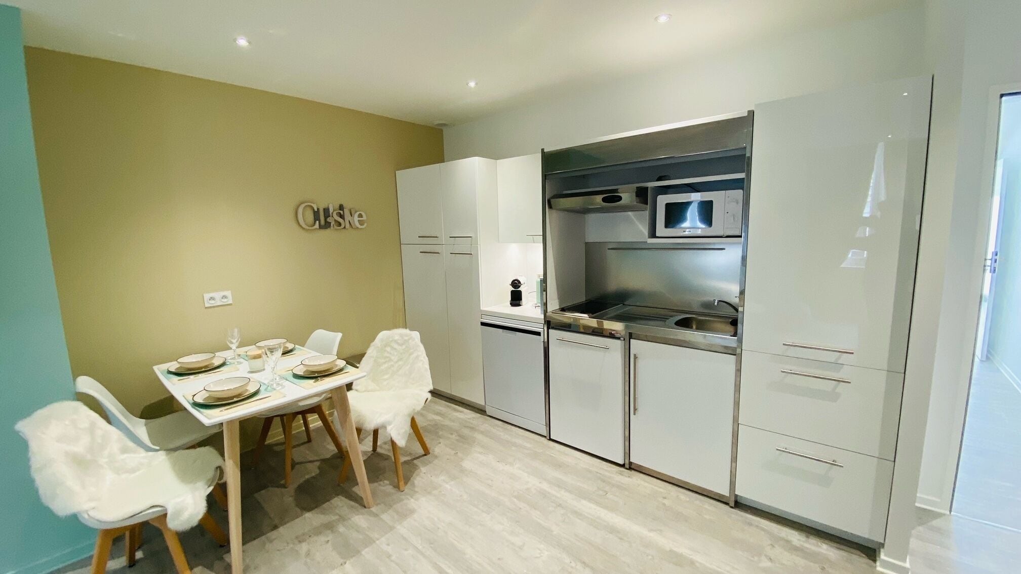 A modern kitchen with white cabinets, a built-in oven, and a dining area with a table set for four.