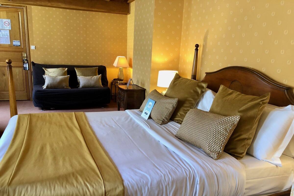 A hotel room with a large bed, a sofa, a nightstand, and a lamp.
