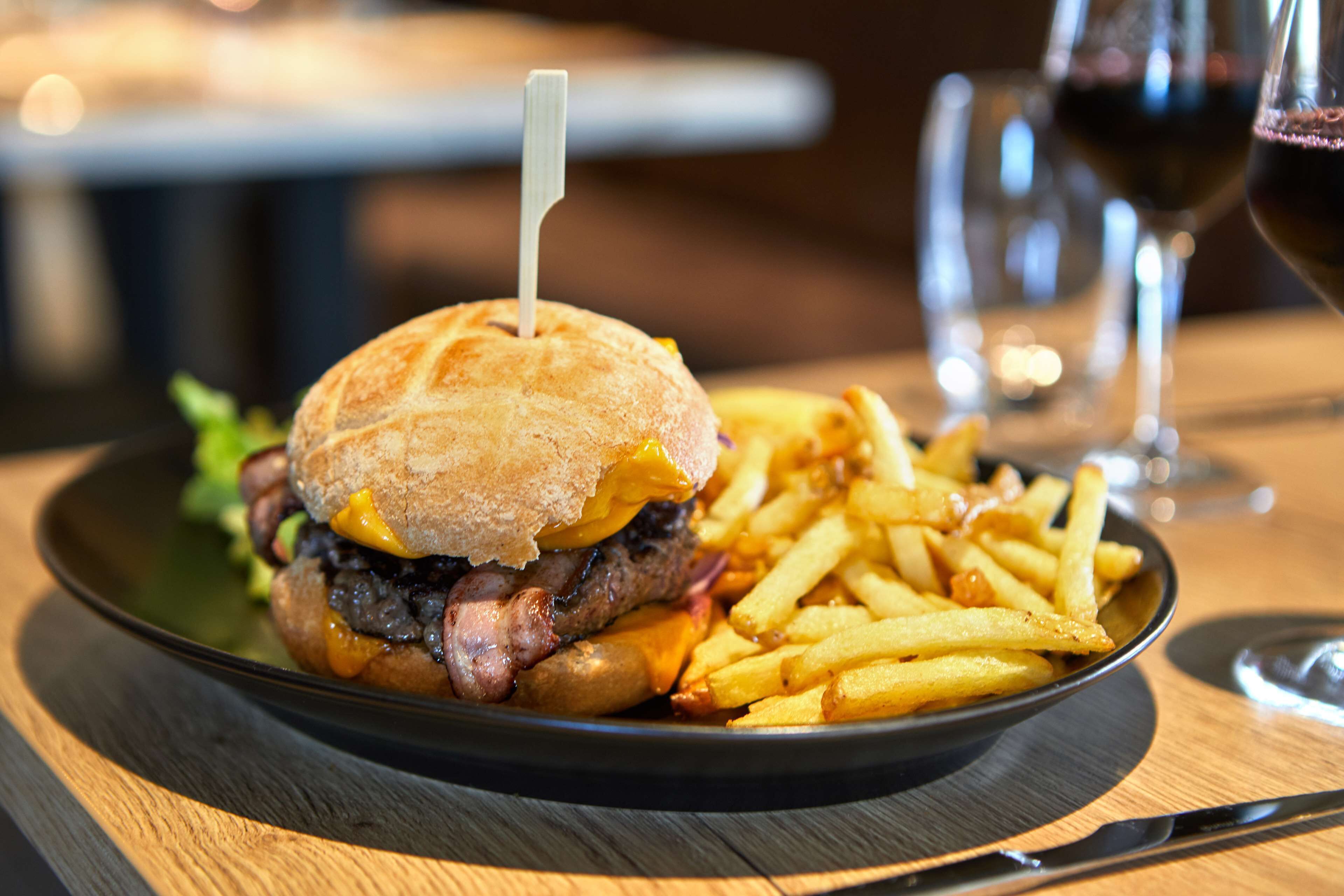 Ein Teller mit einem Burger und Pommes, ein Glas Rotwein und ein Messer auf einem Holztisch.