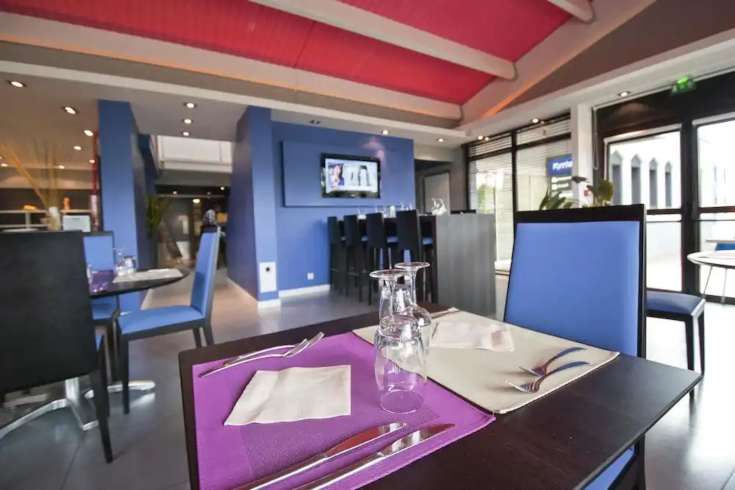 A restaurant with blue chairs and a table set with a purple placemat, clear glasses, and cutlery.