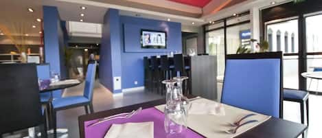 A restaurant with blue chairs and a table set with a purple placemat, clear glasses, and cutlery.