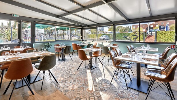 A restaurant with multiple tables and chairs, large windows, and a patterned floor. - Kyriad La Roche Sur Yon (La Roche-sur-Yon)