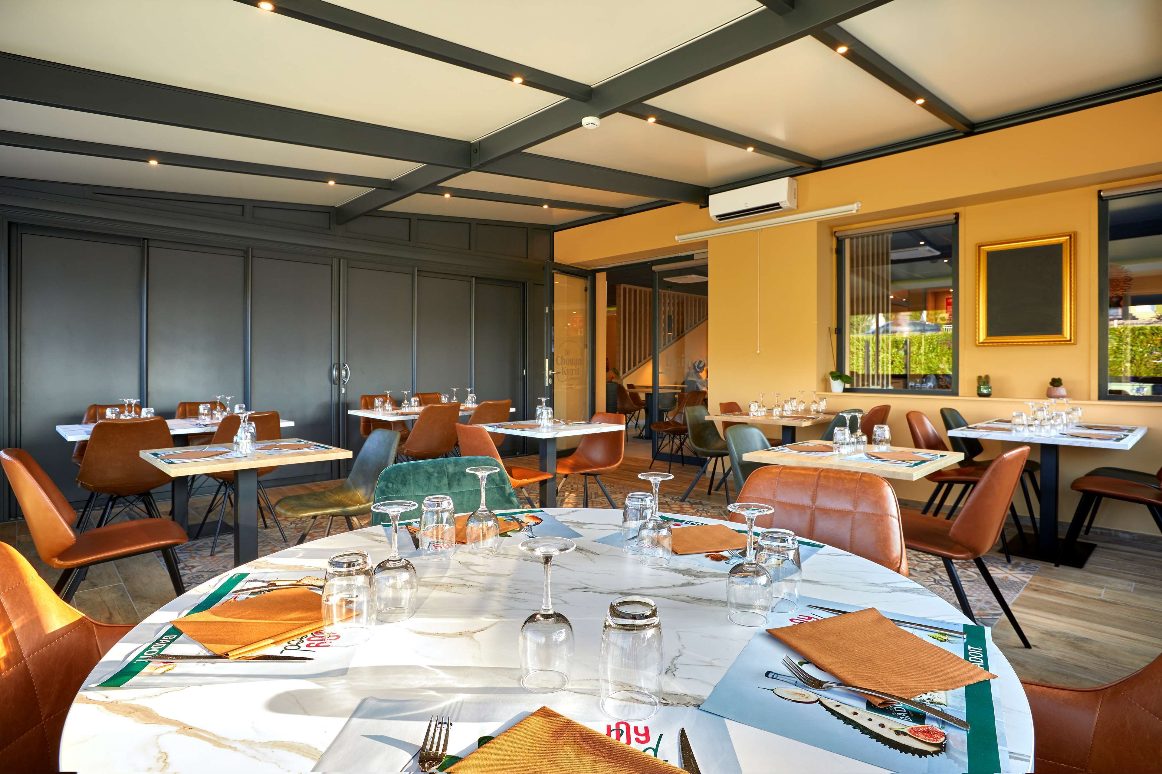 A restaurant with round tables, orange chairs, and a modern interior design.