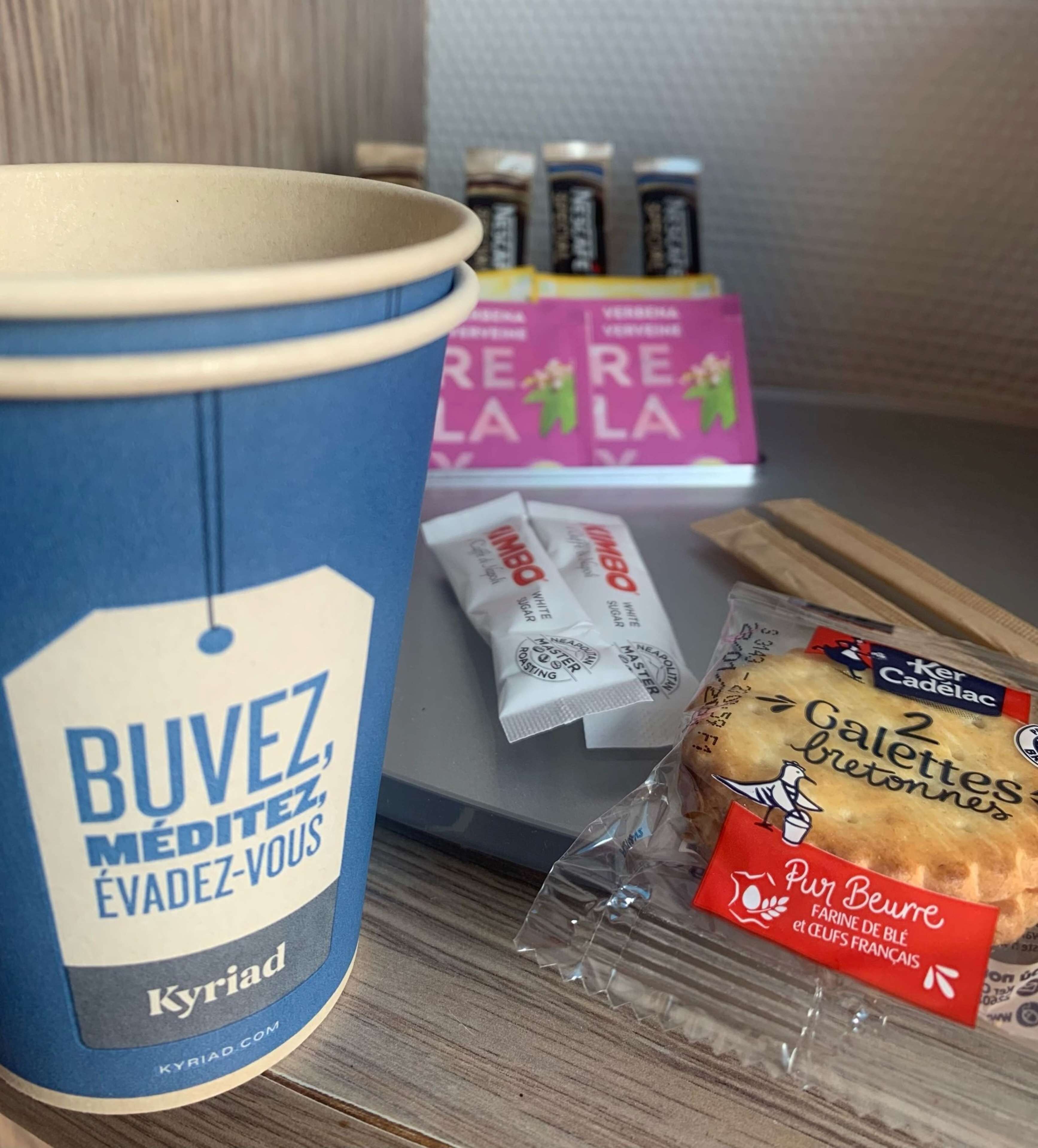 A coffee cup, packets of instant coffee, a loaf of bread, and a box of pastries on a table.