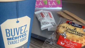 A coffee cup, packets of instant coffee, a loaf of bread, and a box of pastries on a table.