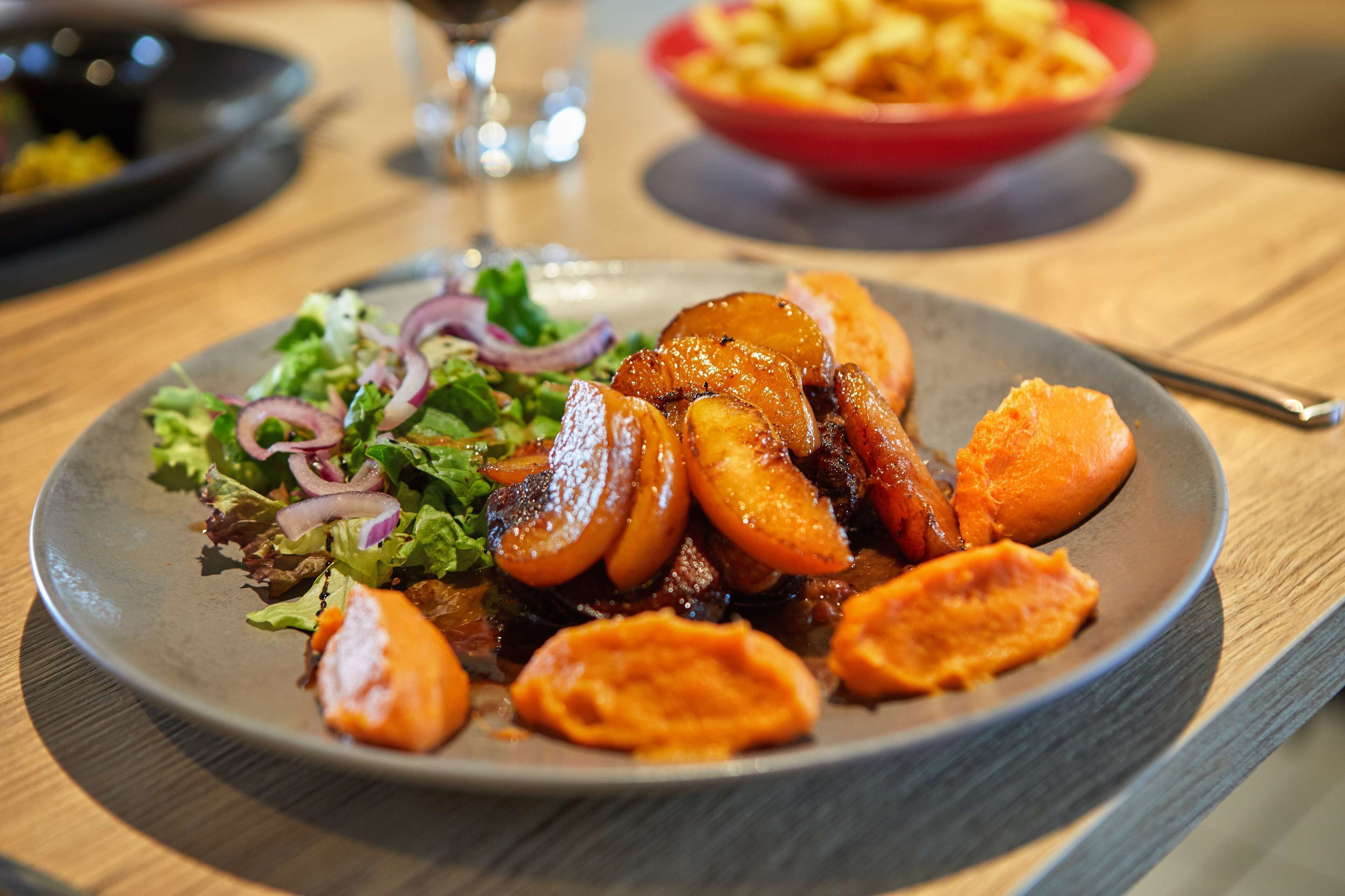 A plate of food with roasted vegetables and a salad on a wooden table.