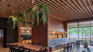 A modern dining area with a wooden table and chairs, a seating area with a bench, and a wall of shelves with decorative items. - Urbana Langsuan Hotel (Bangkok)