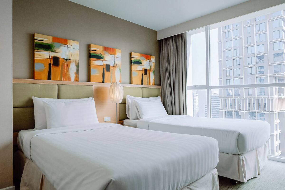 A hotel room with two beds, a large window, and abstract artwork on the wall.