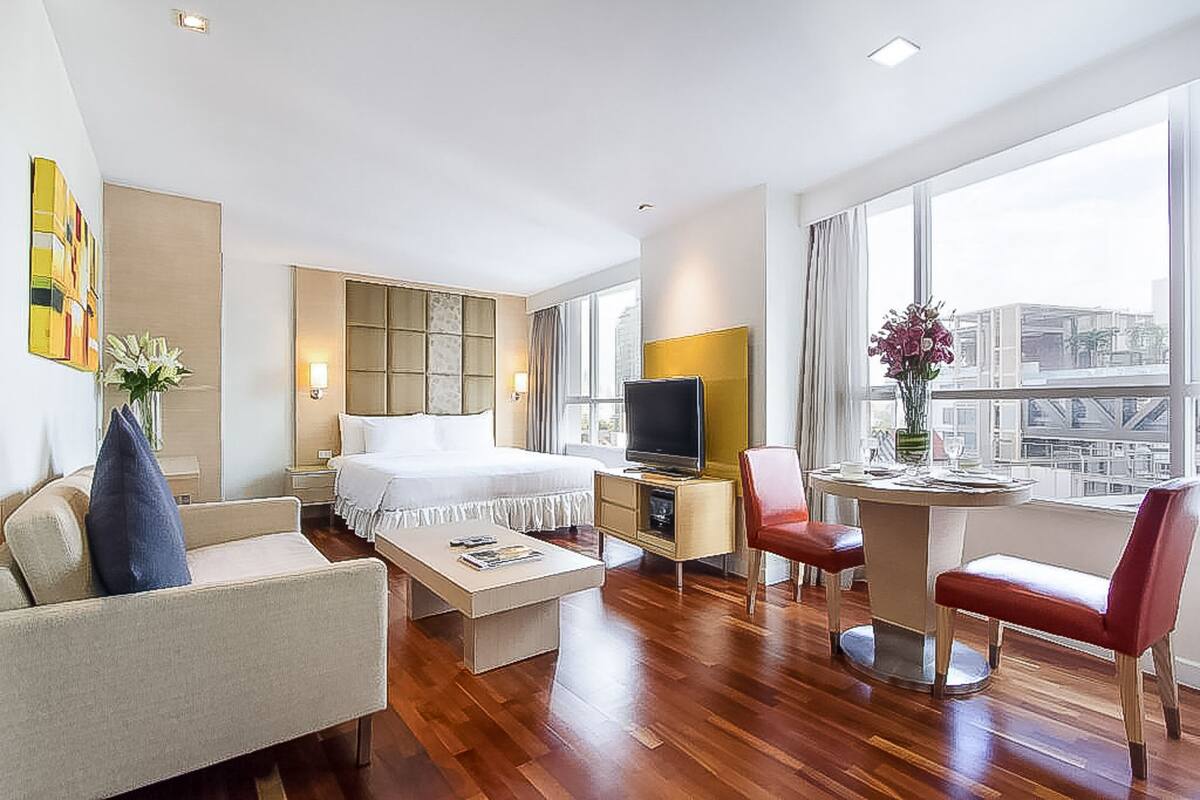 A hotel room with a bed, a TV, a desk, a chair, and a window with a city view.