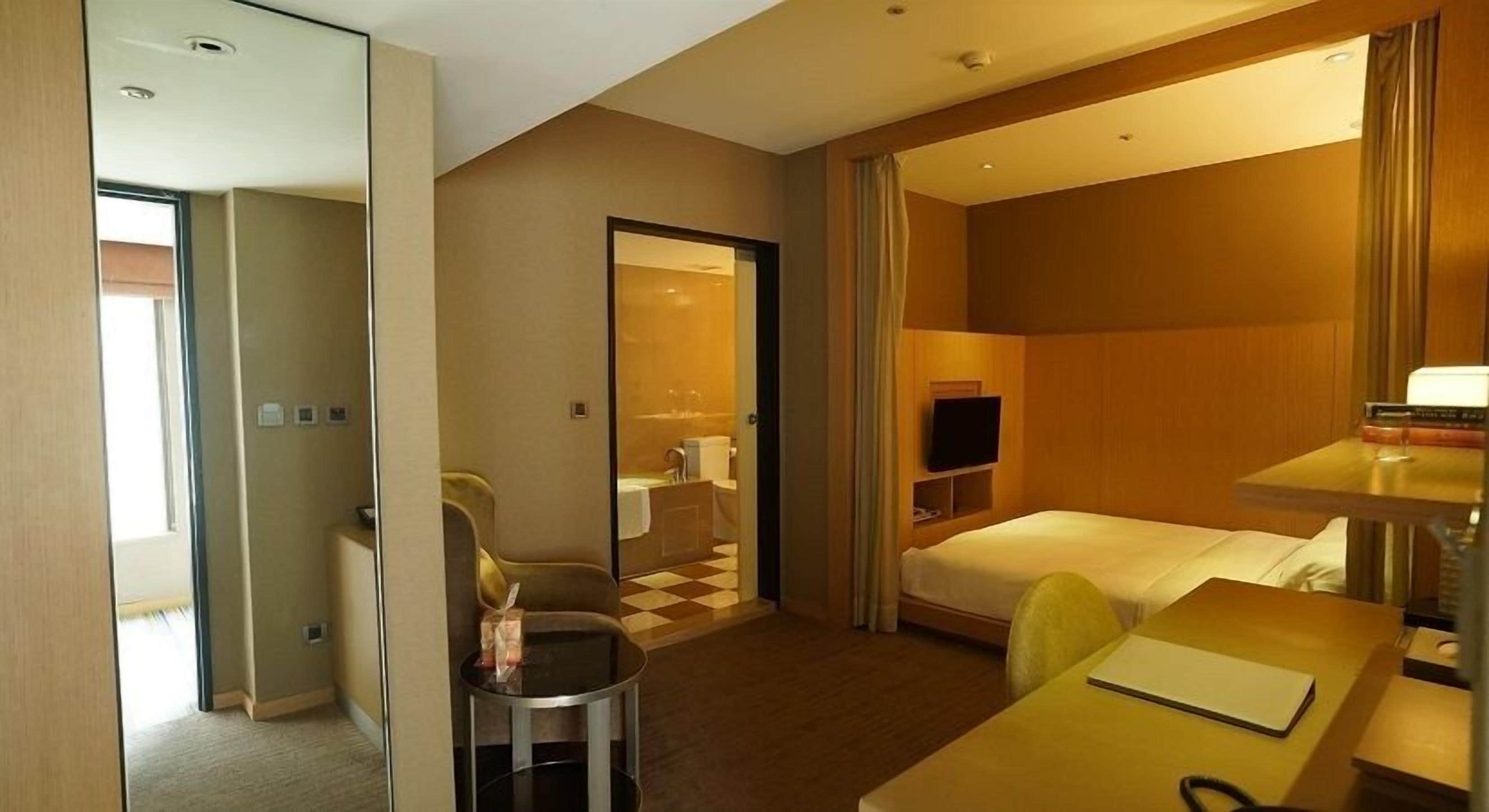 A hotel room with a bed, a desk, a chair, a TV, and a mirror.