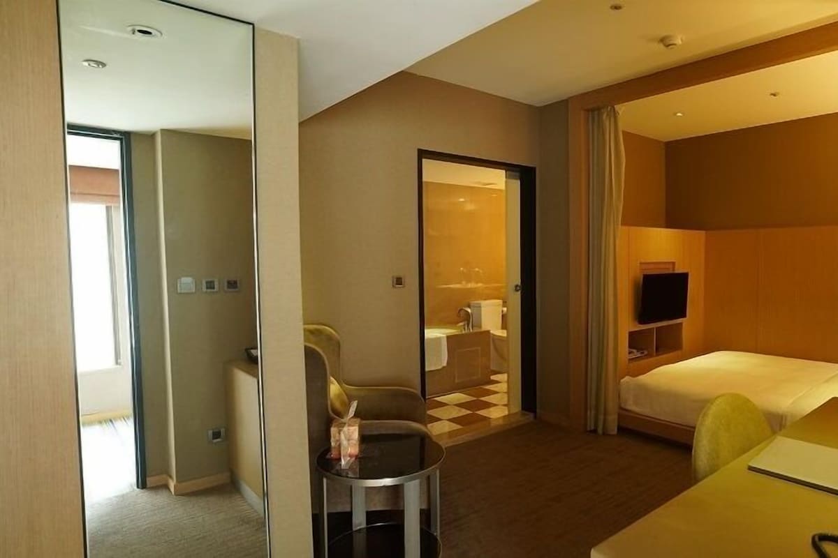 A hotel room with a bed, a desk, a chair, a TV, and a mirror.