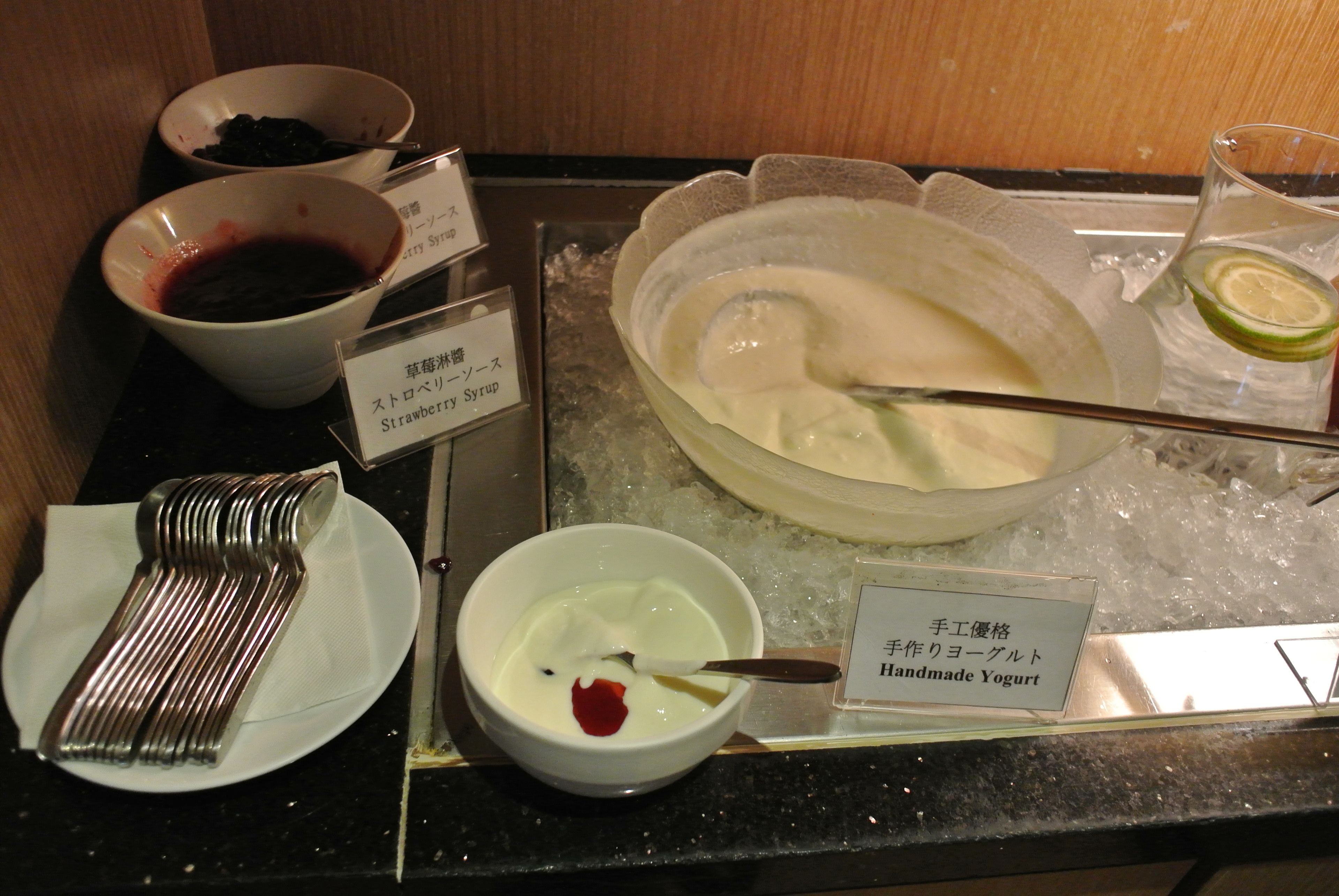 A buffet with various food items including strawberry syrup, yogurt, and ice cream.