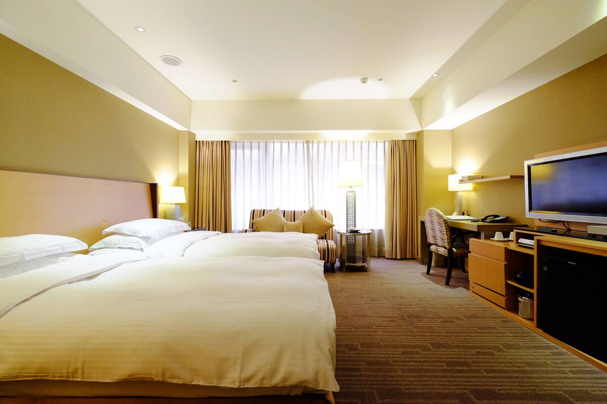 Een hotelkamer met twee grote bedden, een bureau met een computer, een televisie en een minibar.