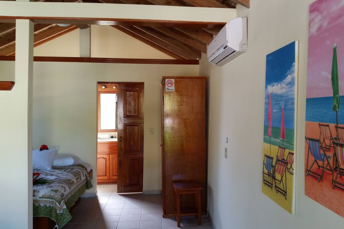 Una habitación con una cama, una mesita, un cuadro de una playa y un cartel de prohibido fumar en la puerta.