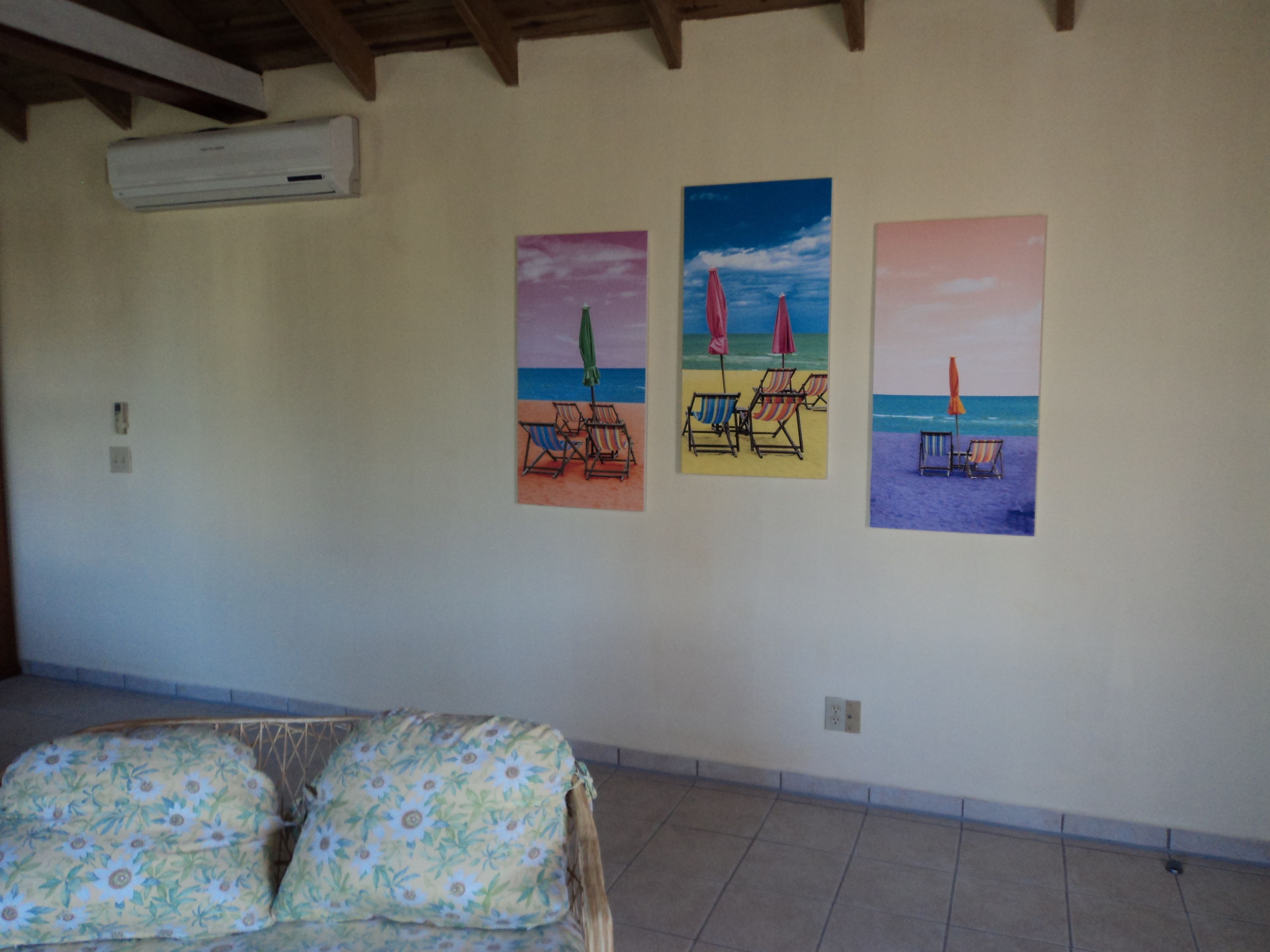 Un dormitori amb un llit, aire condicionat fixat a la paret i tres quadres amb temàtica marina.