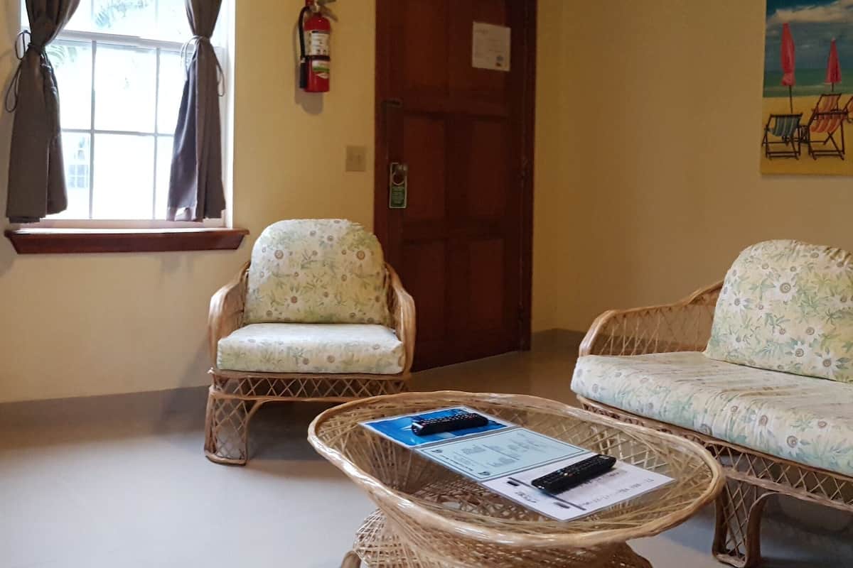 Una sala de estar con sofá, dos sillones, televisor, mesa de centro y ventana con cortinas.