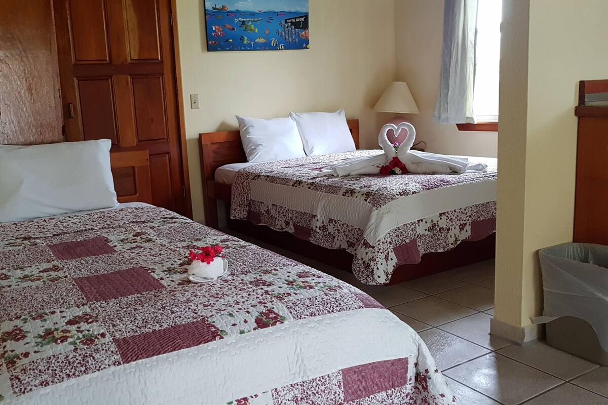 Dos camas individuales con ropa de cama floral, un cabecero de madera, una pintura en la pared y una ventana con cortinas.