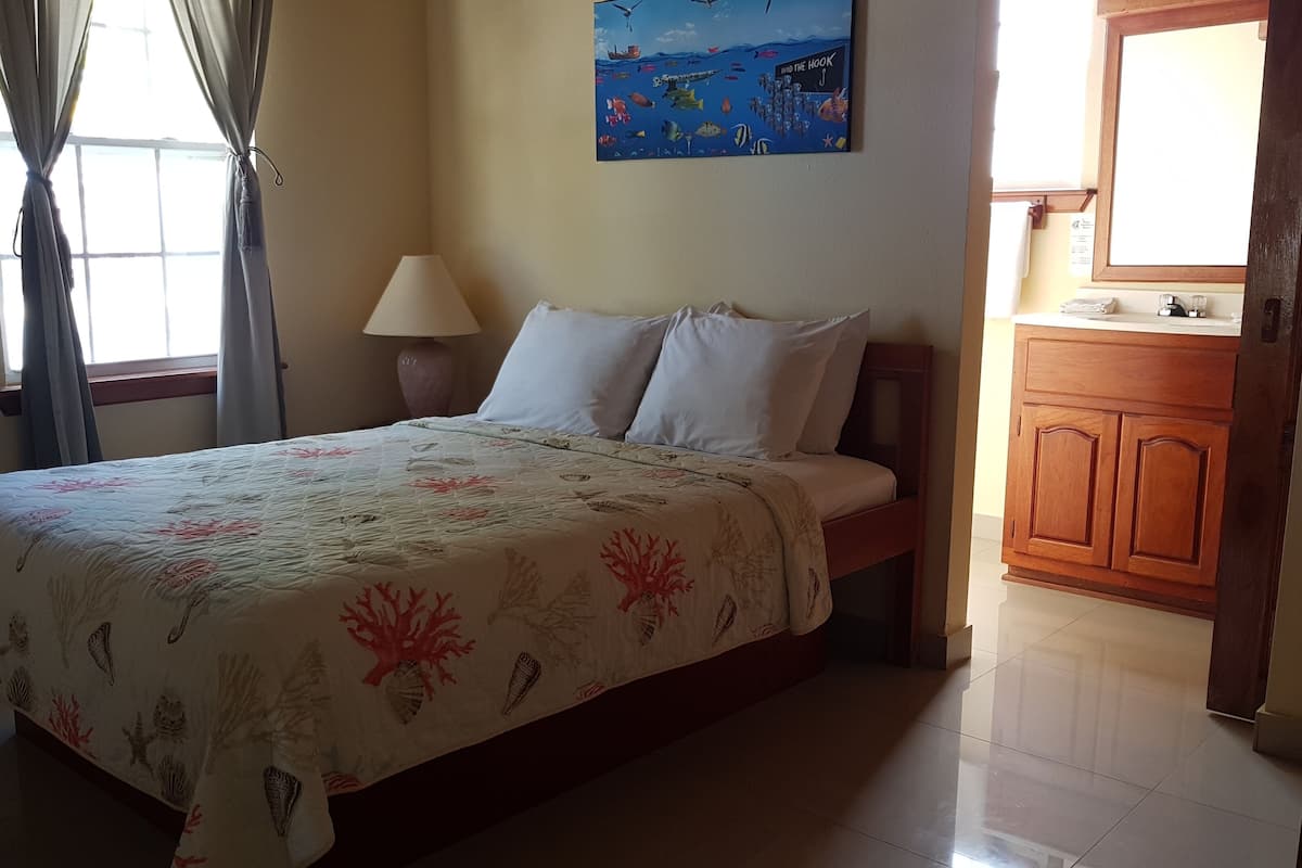 Un dormitorio con una cama, una mesita de noche, una lámpara, un cuadro y un armario de madera.