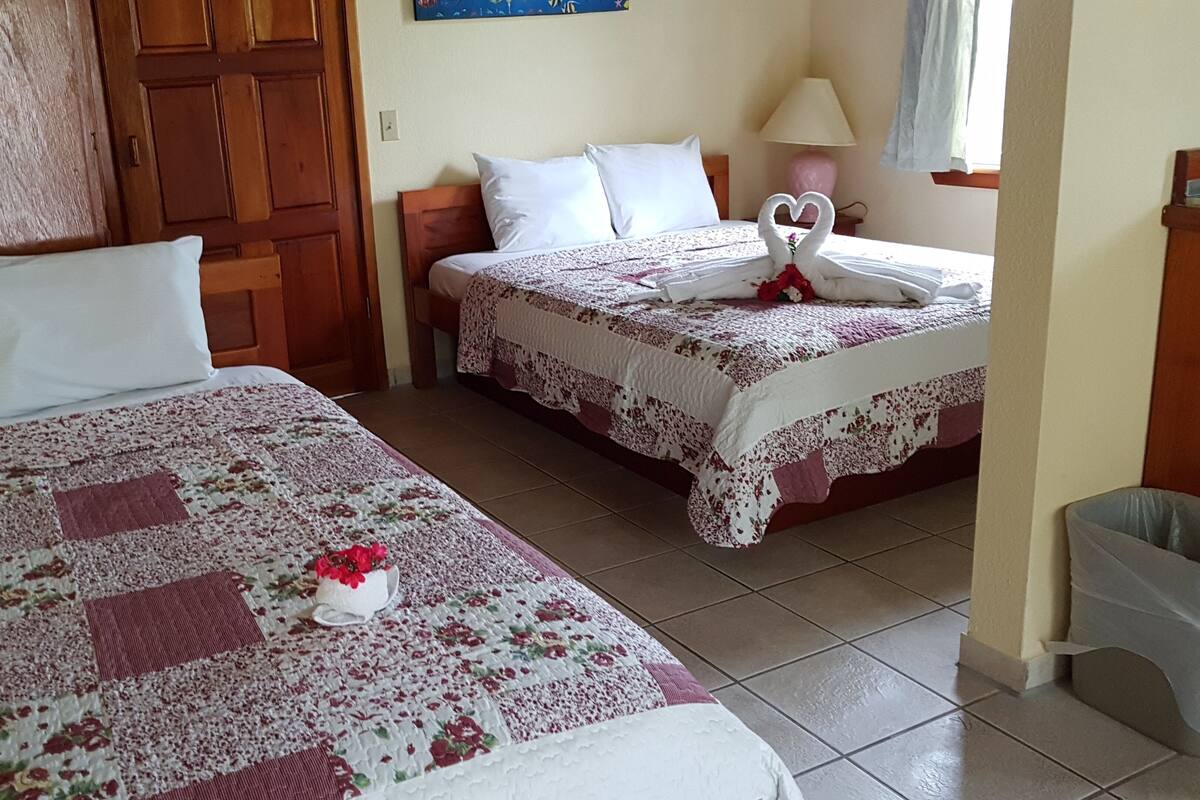 Dos camas matrimoniales con colchas de estampado floral, una puerta de madera y una mesita de noche con una lámpara.