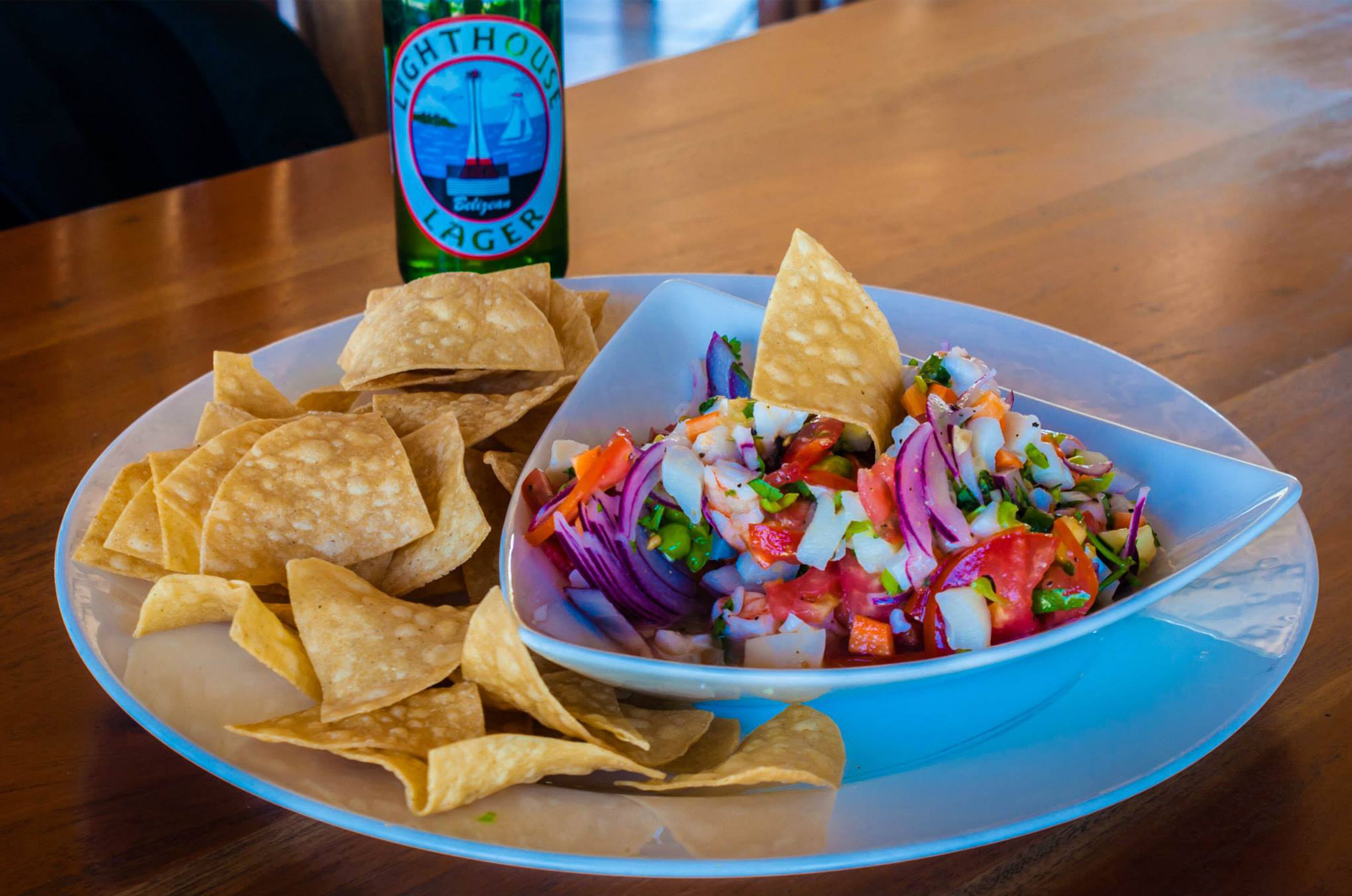 Une assiette de chips de tortillas et un bol de salsa, avec une bouteille de bière en arrière-plan.