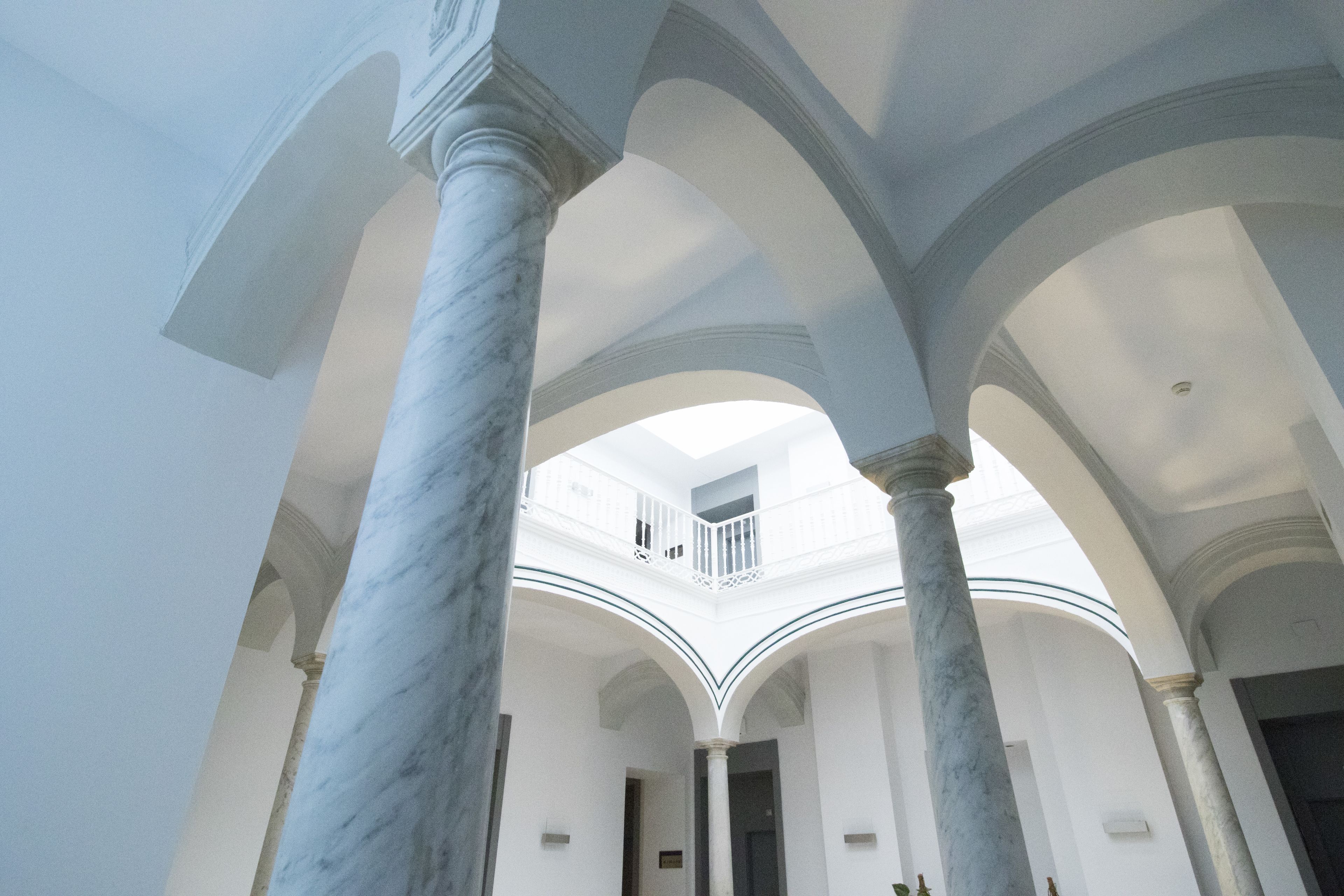 Un interior espacioso con techos altos y columnas de mármol, que cuenta con un área central abierta y un balcón.