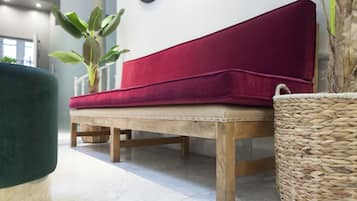Un banco de madera con cojín rojo, una cesta tejida y una planta verde en una habitación moderna con pared blanca y un reloj.