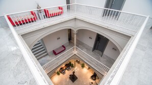 A multi-level atrium with a central seating area, a staircase, and a balcony with red and white patterned sofas. - Petit Palace Santa Cruz (Seville)